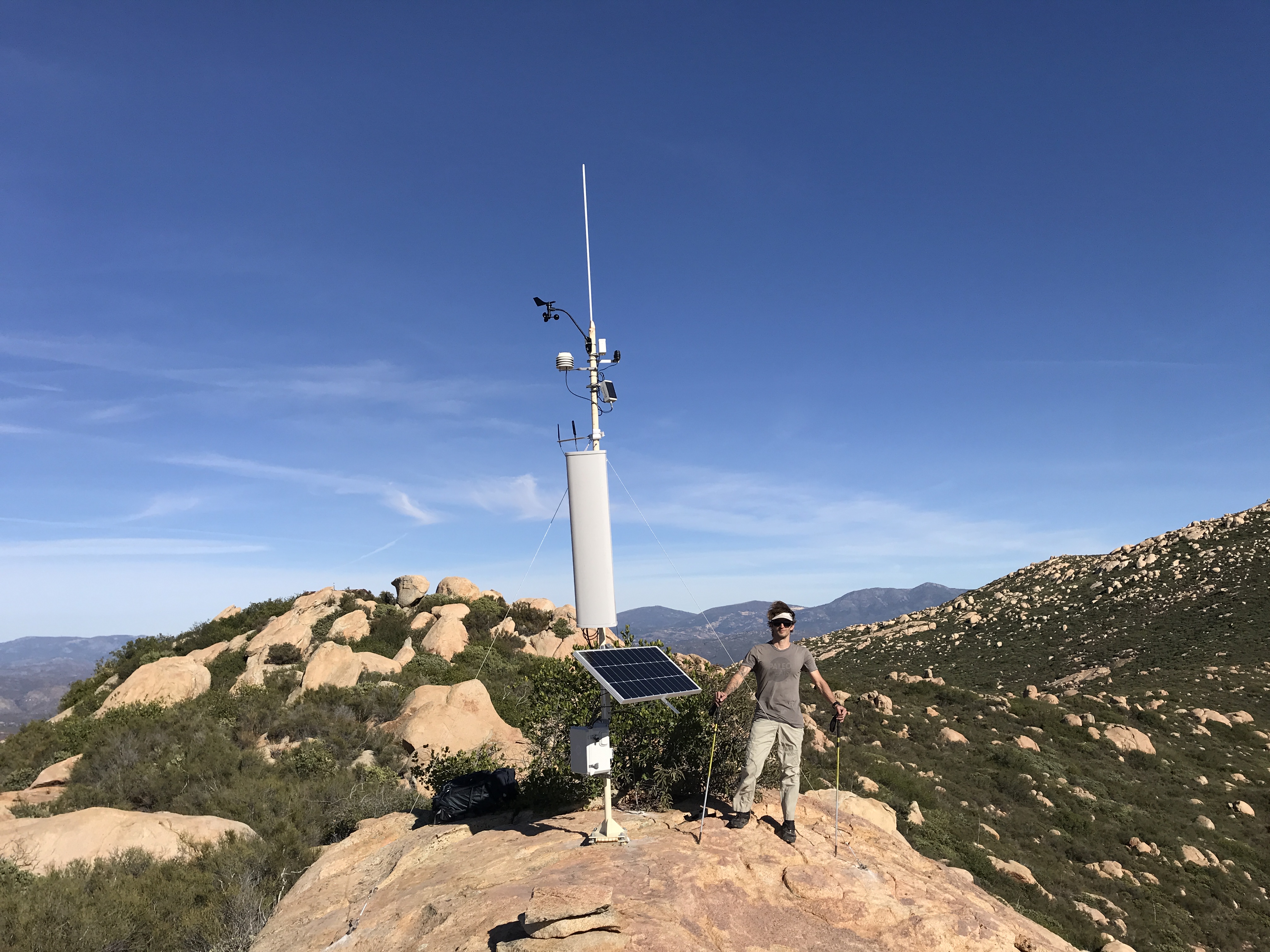 Nik Hawks installing a LoRaWAN IoT Gateway with a sector antenna and weather station on a mountain for long-range remote sensing coverage